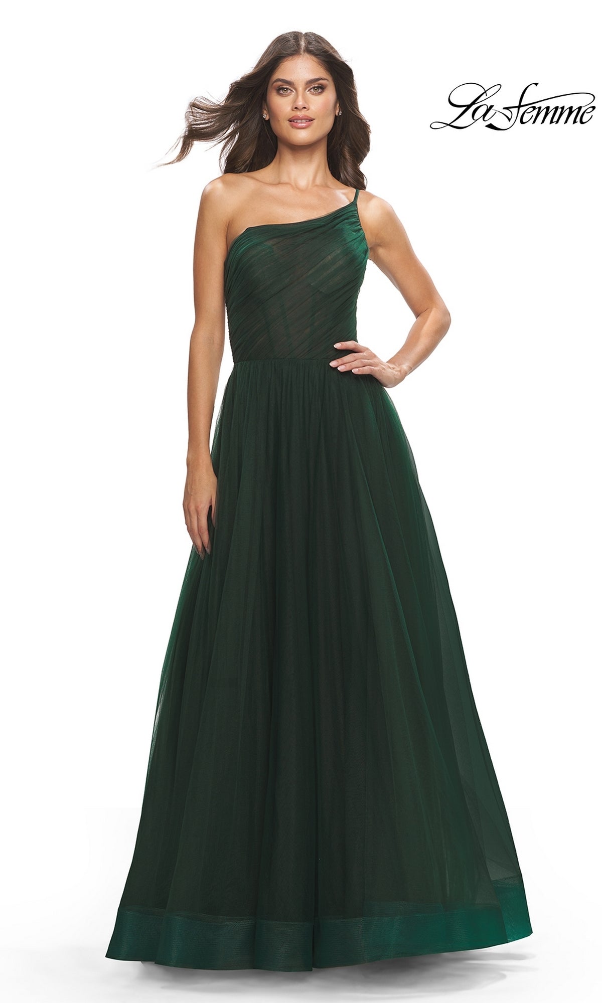 A woman poses against a white background in the One-Shoulder Sheer-Bodice Prom Ball Gown 31069 by La Femme, featuring a dark green fitted bodice and flowing skirt. The elegant look is enhanced by the